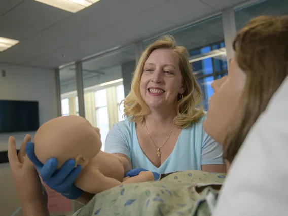 Physician midwife in simulated birthing suite delivering a simulated birth.