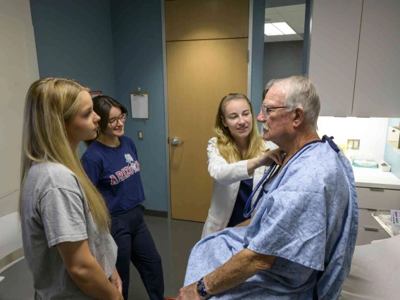 Female medical instructor working with students and patient in clinical setting.