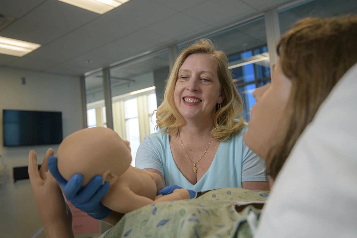 Physician midwife in simulated birthing suite delivering a simulated birth.