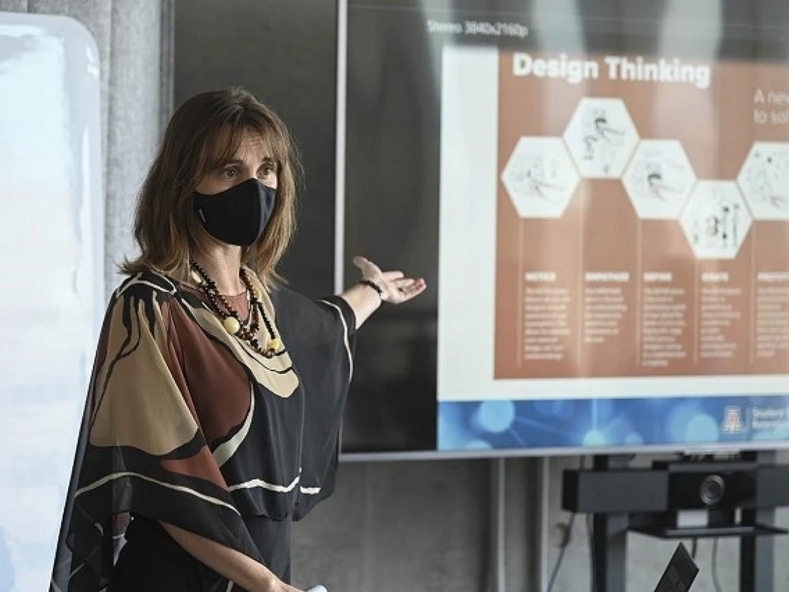 woman wearing a mask gesturing towards a presentation visual with her hand