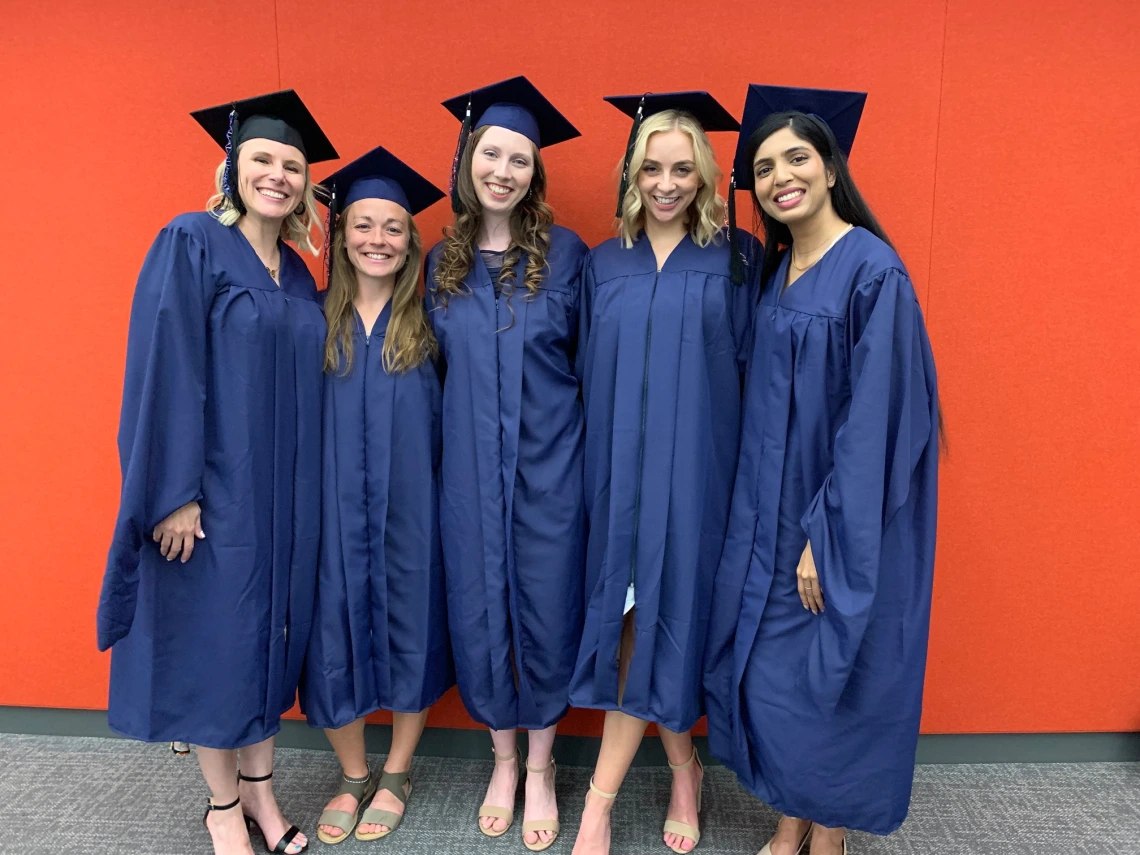 The five 2023 Genetic Counseling program graduates pose together in front of an orange wall