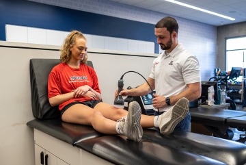 Male physical therapy faculty using ultra-sound on a female patient's leg.
